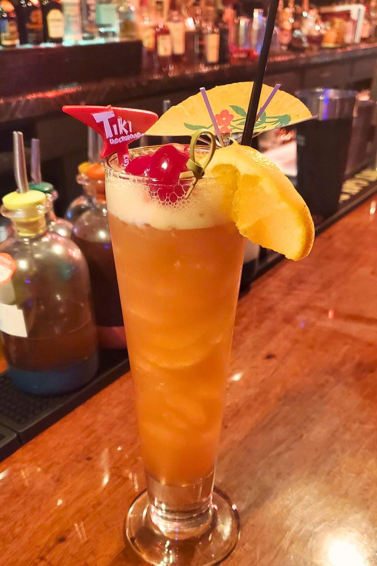 orange cocktail with cherries lemon slice and umbrella garnish at Tiki Underground