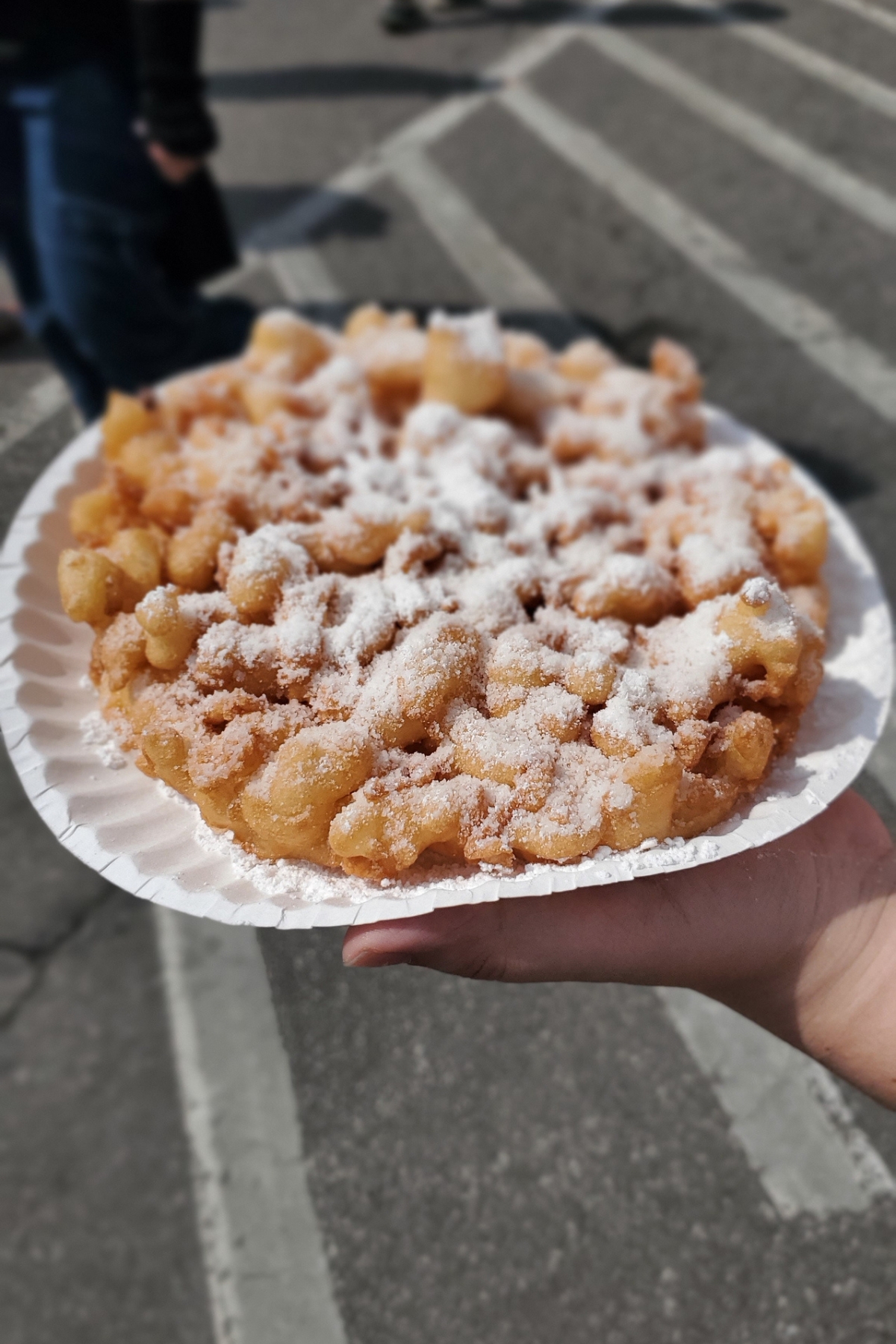 county fair funnel cake with powdered sugar on top on a white paper plate